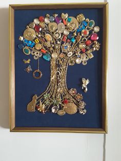 a tree with lots of different types of buttons and charms in a gold frame on a white wall