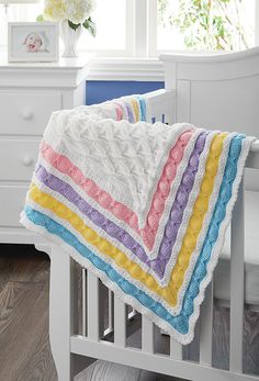 a crocheted baby blanket with multicolored stripes on it in a white crib