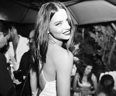 black and white photograph of a woman smiling at an outdoor event with other people in the background