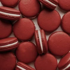 red macaroons with white stripes on them are scattered together in a pile,