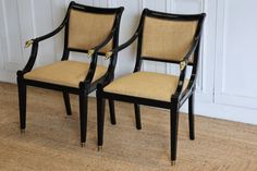 two black chairs sitting next to each other on top of a wooden floor in front of a white wall