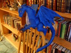 a blue dragon figurine sitting on top of a wooden rocking chair in front of a bookshelf