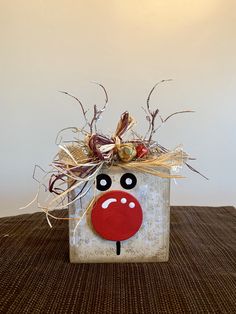 a small square box with a reindeer face on it's side and some dried grass in the background