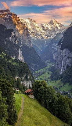 the mountains are covered in green grass and trees, with a small house on top