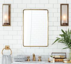 a bathroom with white tile, gold fixtures and a large mirror on the wall above it