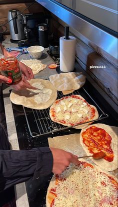 three people making pizzas on top of an oven with dough and sauce in front of them