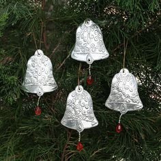 four silver bells hanging from a tree with red bead trimming on it's sides