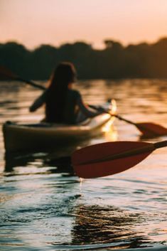 two people in kayaks paddling on the water at sunset