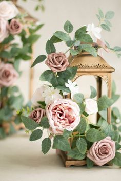 some pink flowers and green leaves on a white tablecloth with a small lantern in the background