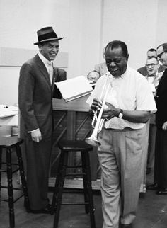 two men standing next to each other in front of a group of people with musical instruments