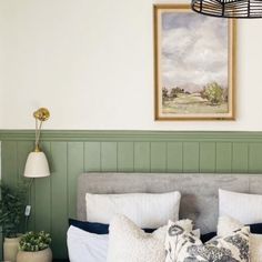 a bedroom with green paneling and white bedding, two plants on the nightstands