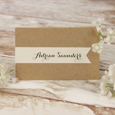 an image of a place card with flowers on the wooden table and white petals around it