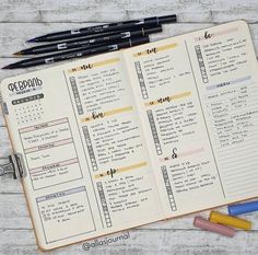 an open planner with pens and markers next to it on top of a wooden table