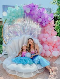 a woman and her daughter sitting on an inflatable chair with balloons behind them