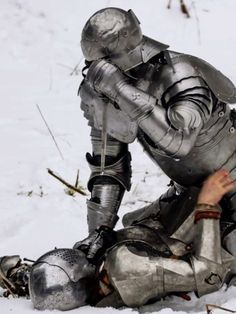 a man dressed in armor kneeling down in the snow with his foot on the ground