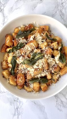 a white bowl filled with pasta covered in parmesan cheese and green beans on top of a marble counter