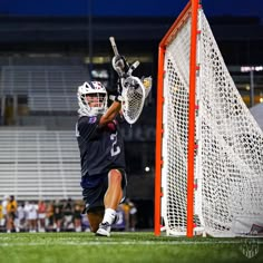 a lacrosse goalie in action on the field at night with fans watching from the bleachers