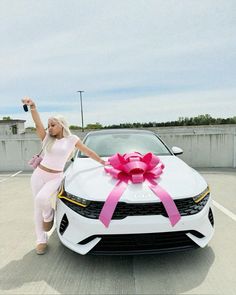 a woman standing next to a white car with a pink bow on it's hood