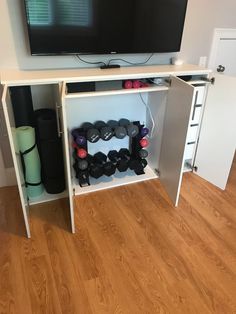 a tv mounted on top of a white cabinet filled with dumbs and exercise equipment