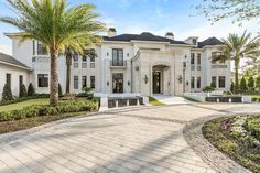 a large white house with palm trees in the front yard and landscaping on either side