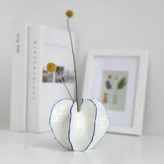 a white vase with two yellow flowers in it on a table next to a book