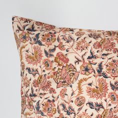 a decorative pillow with an orange and blue floral pattern on it's side, sitting against a white wall