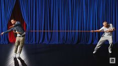 two men in front of a blue curtain, one pulling the string with his hands