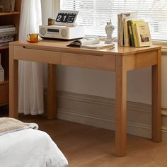 a wooden desk with books and an alarm clock on it in front of a window