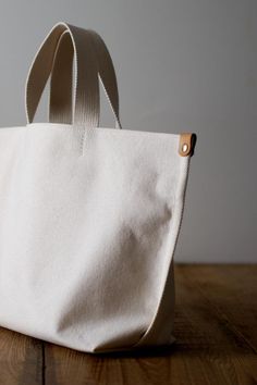 a white canvas bag sitting on top of a wooden table next to a black object