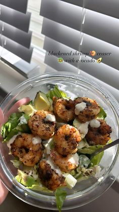 a person holding a glass bowl filled with shrimp and lettuce, topped with ranch dressing