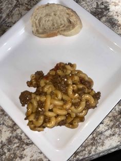 a white plate topped with pasta next to a piece of bread on top of a counter