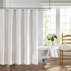 a white shower curtain in a bathroom next to a bathtub and chair with flowers on the floor