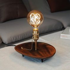 a light bulb sitting on top of a wooden table next to a white bed with pillows