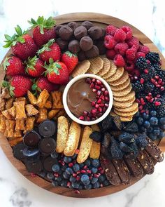 a wooden platter filled with fruit, crackers, and chocolate covered strawberries