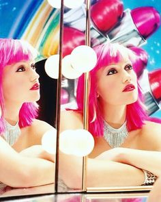 a woman with pink hair is looking at herself in the mirror and she has her arms crossed