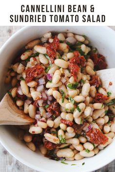 a white bowl filled with beans and tomato sauce next to a wooden spoon on top of a table