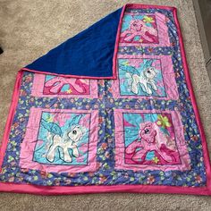 a pink and blue quilted blanket with ponys on it, laying on the floor