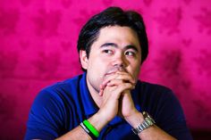 a man sitting in front of a pink wall with his hands on his chin looking up