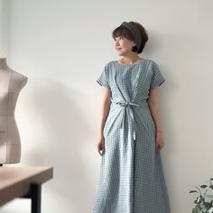 a woman standing in front of a white wall wearing a blue dress and headband