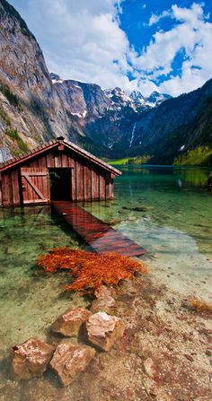 an old wooden boathouse in the middle of a lake with mountains in the background