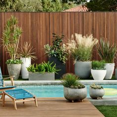 a wooden deck next to a swimming pool with potted plants and chairs around it