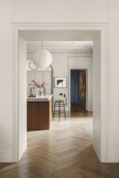 an open door leading to a kitchen and dining room with white walls, wood floors and parquet flooring