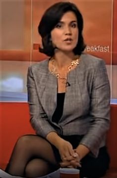 the woman is sitting down talking on her television news set, wearing tights and stockings