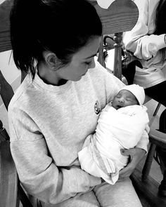 a woman holding a baby in her arms while sitting on a chair with other people