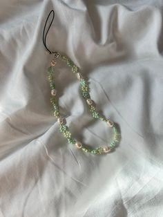 a green beaded necklace laying on top of a white cloth covered bed sheet with a black string attached to it