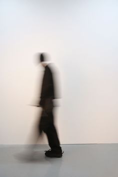 a blurry image of a man walking in front of a white wall