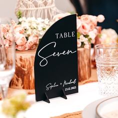 a table sign sitting on top of a wooden stand next to glasses and napkins