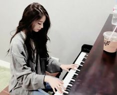 a woman sitting at a piano with a drink in her hand and playing the piano