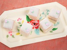 four square pieces of cake sitting on a plate with flowers and leaves painted on it