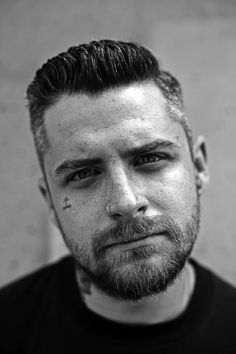 a black and white photo of a man with tattoos on his face looking at the camera